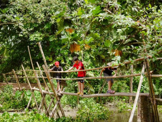 Vietnamese countryside children crossing a traditional monkey bridge with remarkable ease, showcasing a daily routine in the region on can tho city tour