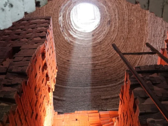 A dramatic shot of light pouring through an opening at the top of a dark, traditional brick kiln