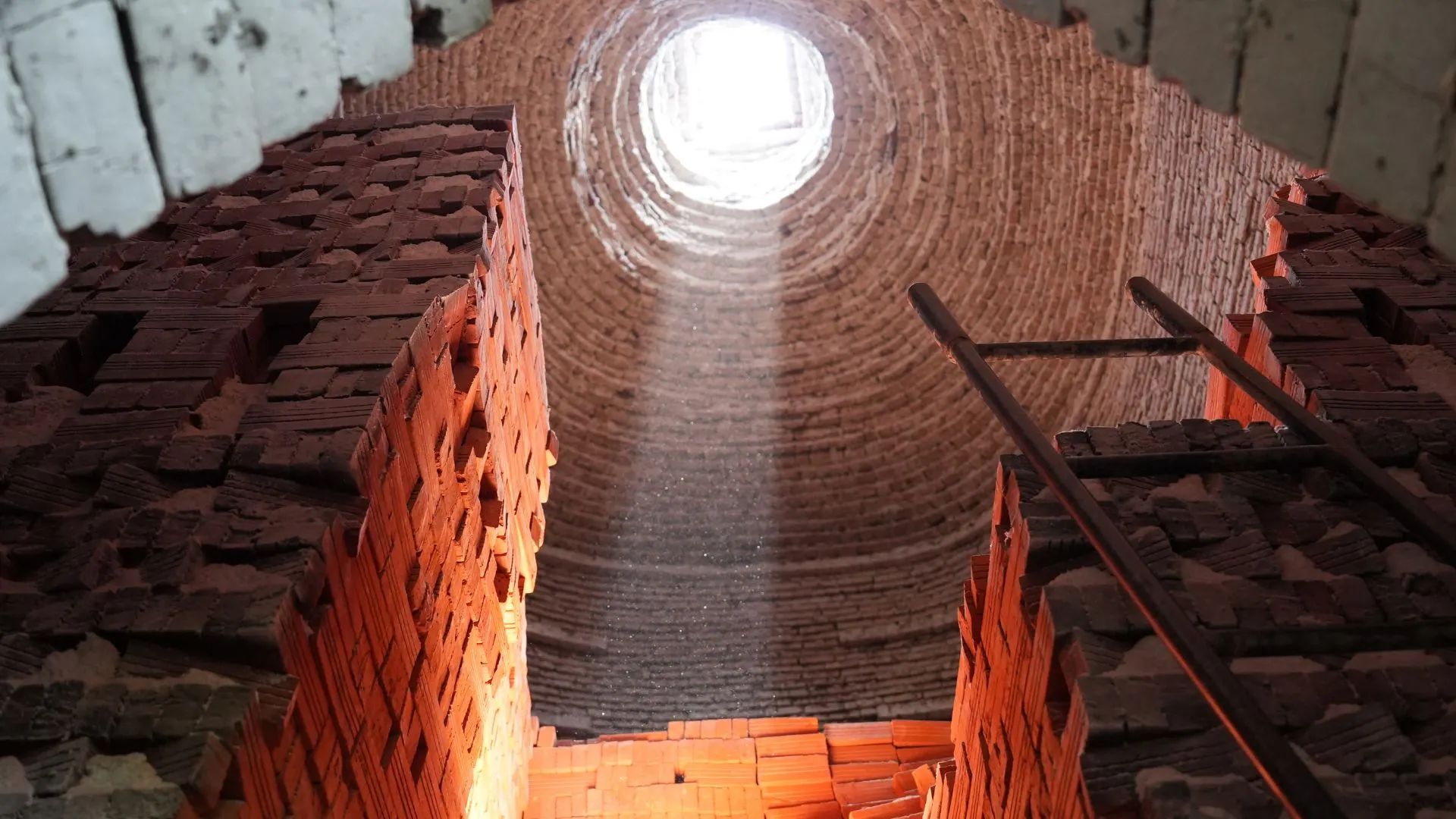 A dramatic shot of light pouring through an opening at the top of a dark, traditional brick kiln