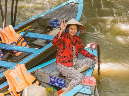 A local woman wearing a traditional conical hat skillfully rowing a small wooden sampan boat