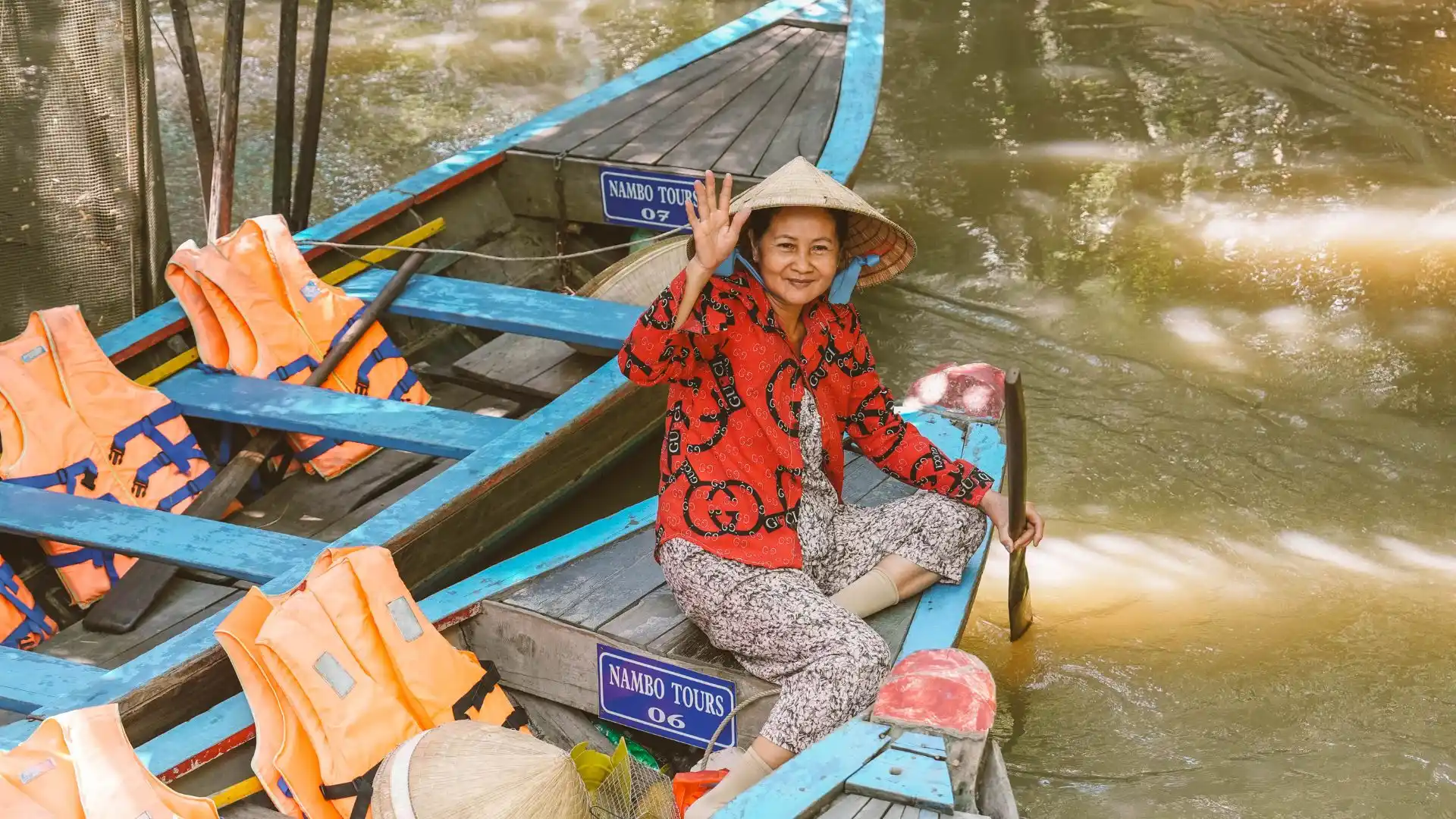 A local woman wearing a traditional conical hat skillfully rowing a small wooden sampan boat