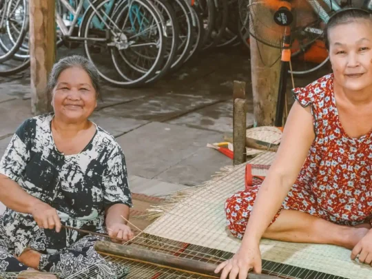 An elderly artisan skillfully weaving a colorful sedge mat on a traditional wooden loom