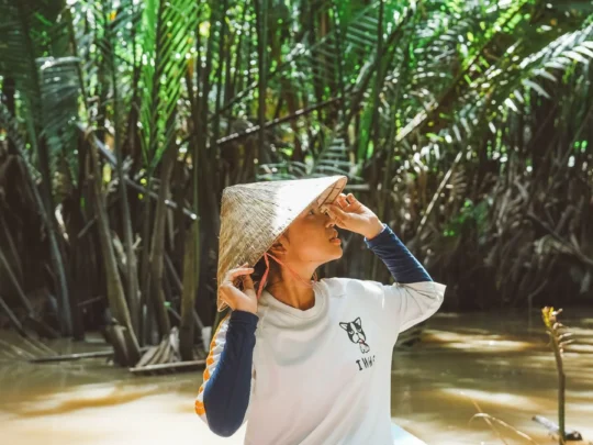 Tourists on a sampan boat weaving through a narrow, picturesque canal shaded by nipa palms