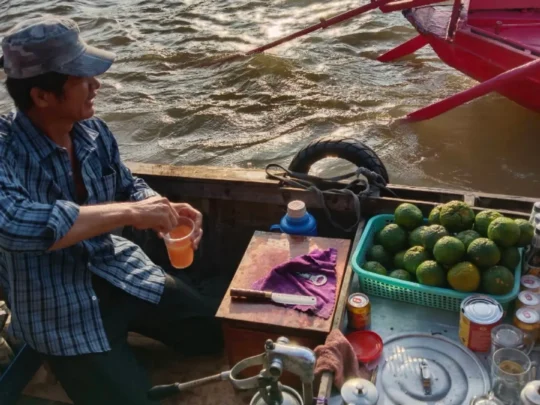 Vendor serving drinks and fruit from a boat at Cai Rang Floating Market
