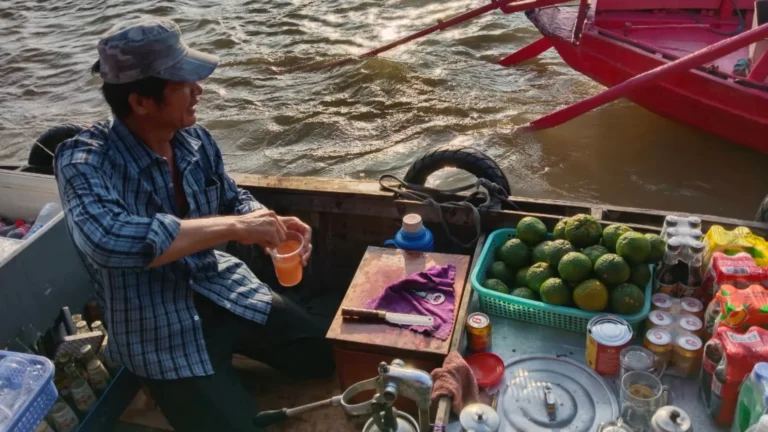 Vendor serving drinks and fruit from a boat at Cai Rang Floating Market