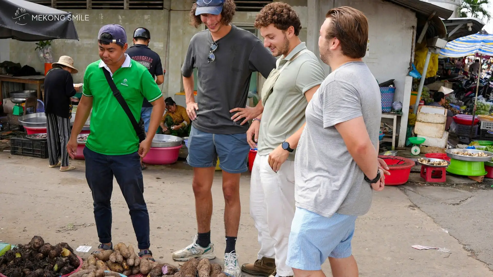 A traveler and guide buying fresh vegetables and herbs from a vendor at a traditional market for their cooking class.