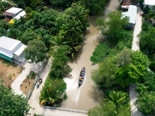 An aerial view of a winding canal in the Mekong Delta, surrounded by lush green vegetation, Cai Rang floating market tour