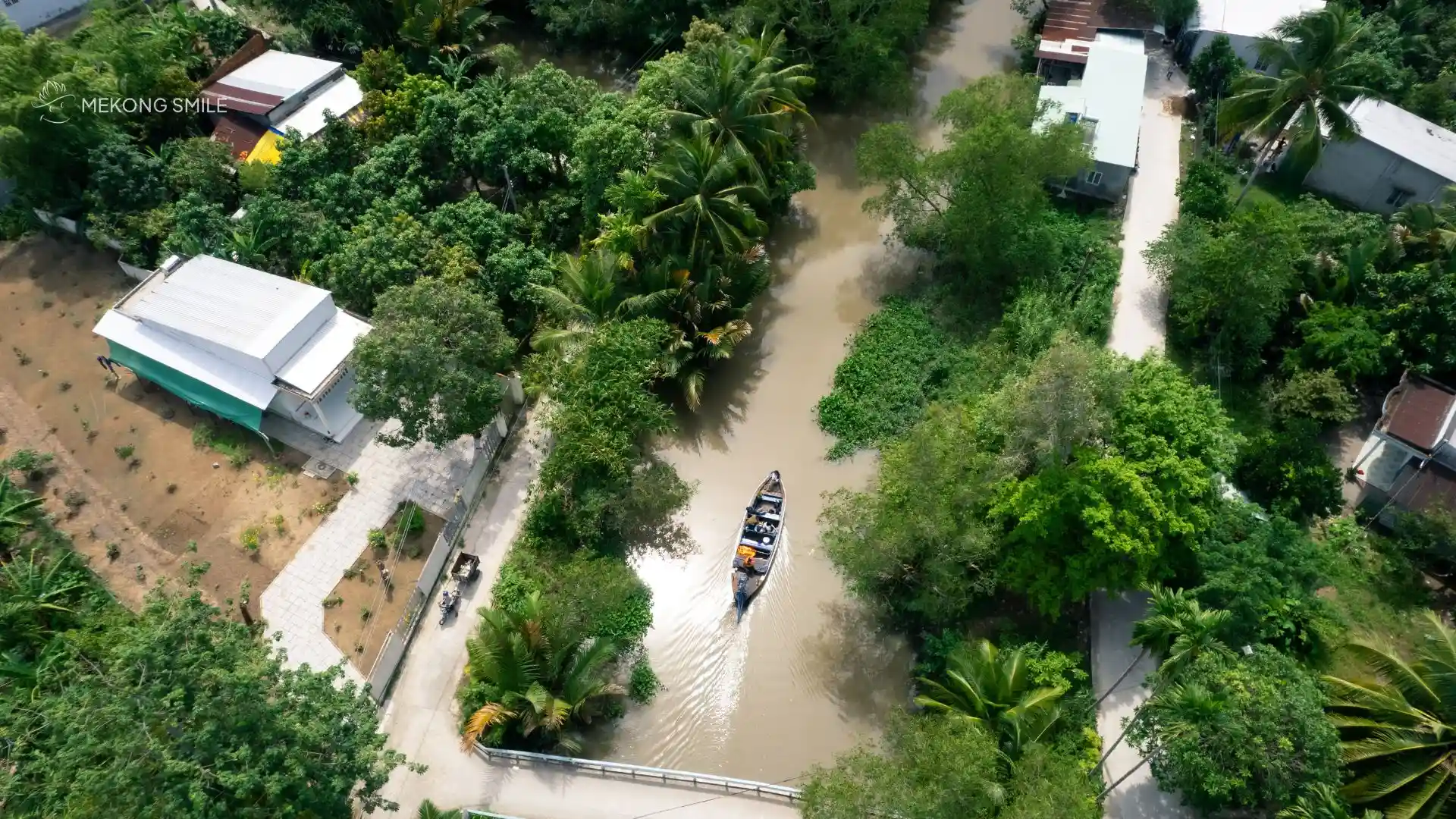 An aerial view of a winding canal in the Mekong Delta, surrounded by lush green vegetation, Cai Rang floating market tour