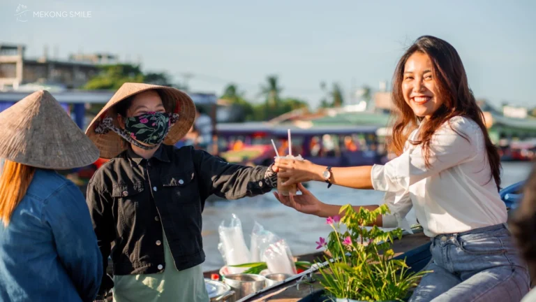 A traveler buying a cup of traditional Vietnamese morning coffee from a small boat on the Cai Rang Floating Market.
