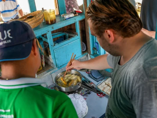 A person frying golden-brown chả giò (Vietnamese fried spring rolls) in a pan during a cooking class.