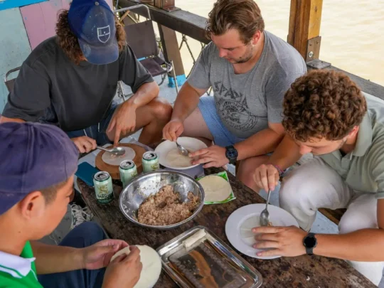 Travelers preparing food together under the careful and enthusiastic guidance of a local instructor.