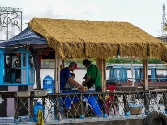 A wide shot of a spacious and open-air area for a cooking class, surrounded by tropical greenery.