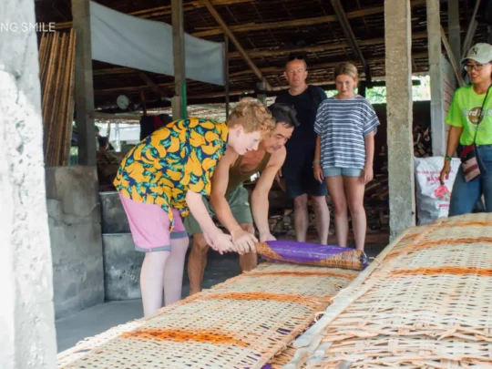 A person carefully spreading rice paper batter into a thin layer on a steaming cloth, in Cai Rang floating market tour