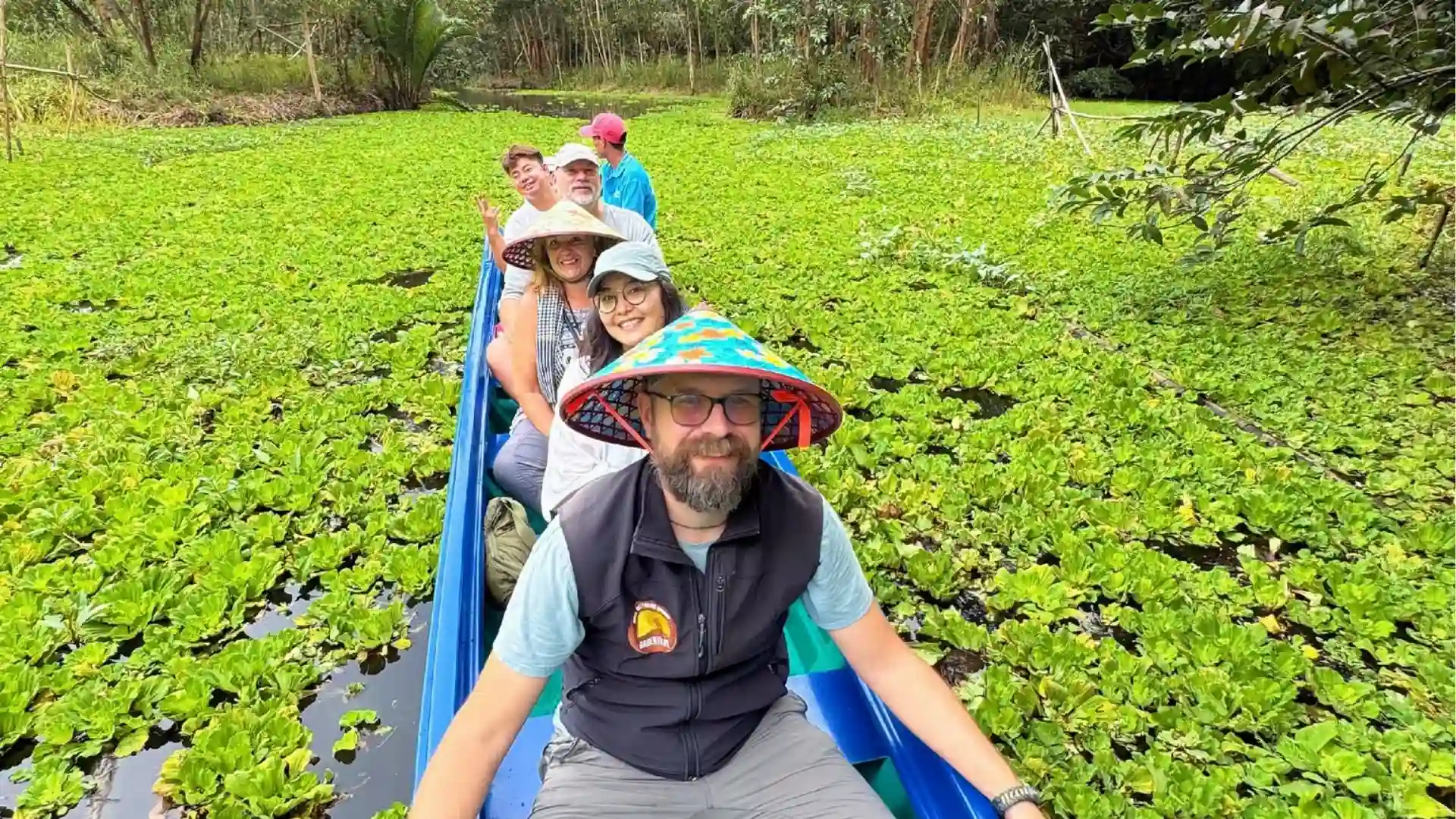 Can Tho Fam Trip 2026: Connecting International Travel Partners with Local Experiences 11 International visitors taking a small boat through a green wetland landscape in Can Tho