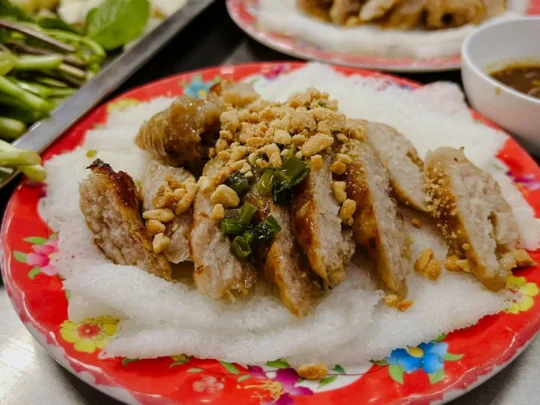 An appetizing plate of freshly grilled Nem Nướng served with fresh herbs, vermicelli, and rice paper.