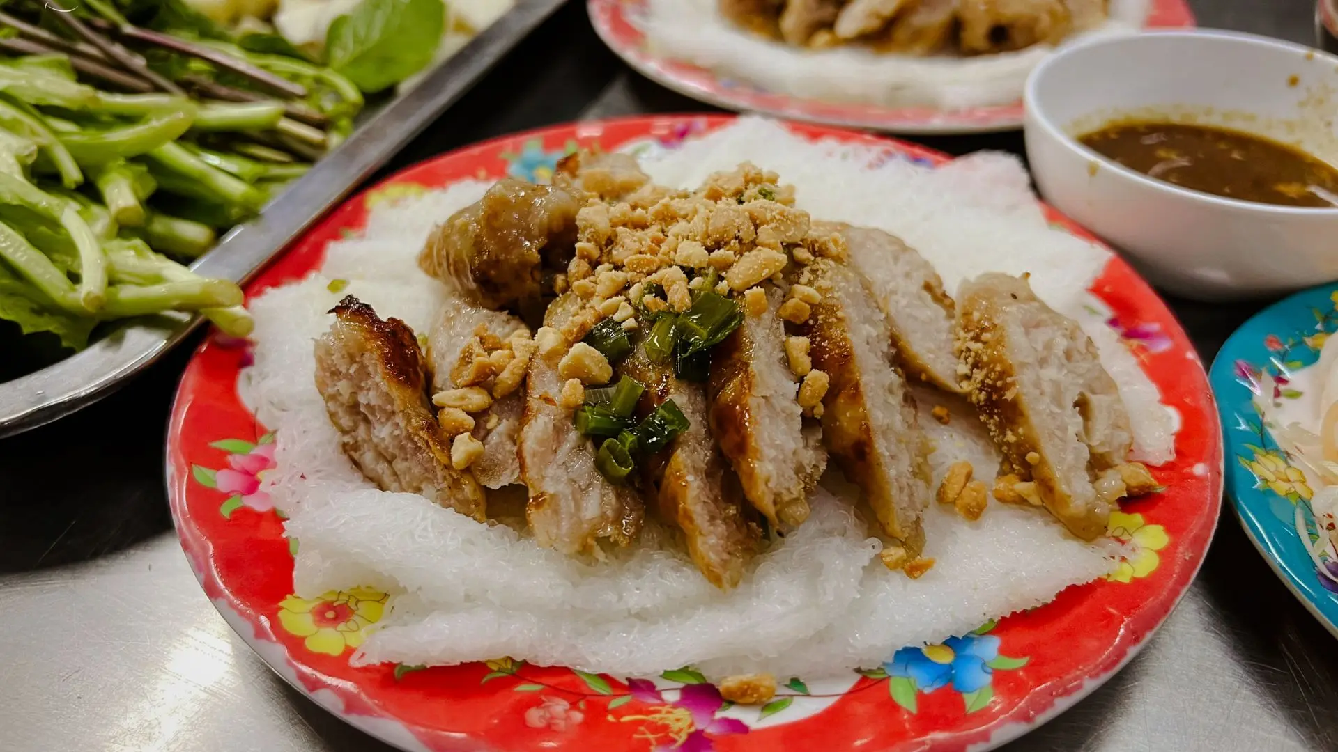 An appetizing plate of freshly grilled Nem Nướng served with fresh herbs, vermicelli, and rice paper.