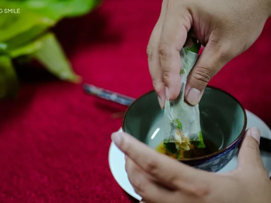A close-up shot of Bánh Cống being dipped fully into a bowl of flavorful fish sauce