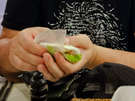 A tourist learning the traditional Vietnamese way of wrapping nem nướng with rice paper and fresh herbs