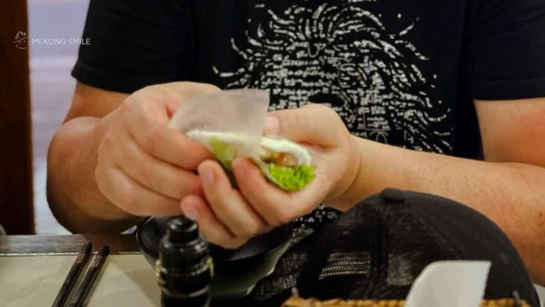 A tourist learning the traditional Vietnamese way of wrapping nem nướng with rice paper and fresh herbs