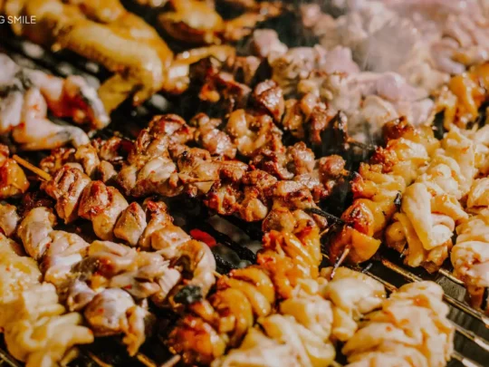Nem Nướng (grilled pork sausage) being cooked over hot charcoal, a popular street food known for its smoky aroma.