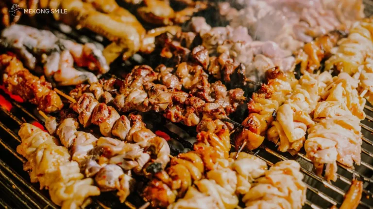 Nem Nướng (grilled pork sausage) being cooked over hot charcoal, a popular street food known for its smoky aroma.