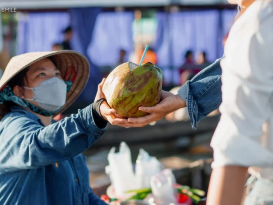 A local vendor passing a fresh coconut to a tourist's boat during the Me Kong Smile tour of Cai Rang floating market