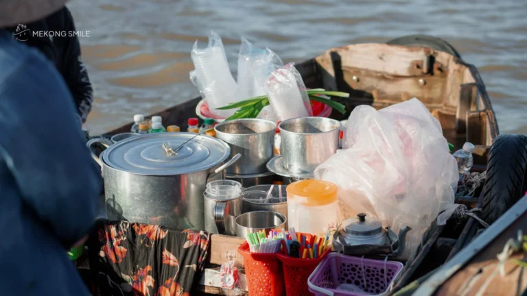 A local vendor preparing a hot bowl of Vietnamese noodle soup on a small floating kitchen boat in Can Tho