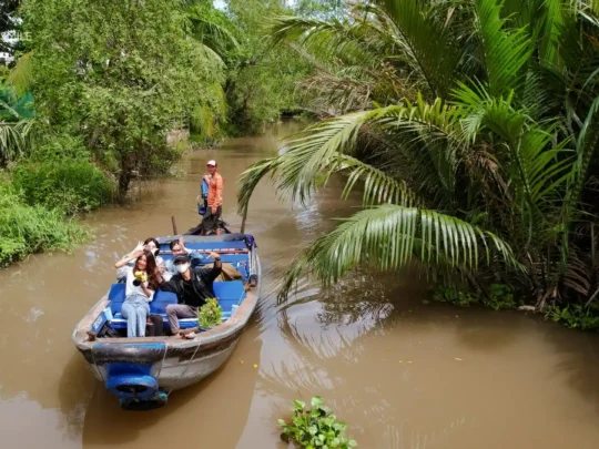 A small sampan boat navigating through a narrow, secluded green canal in Can Tho River Tour