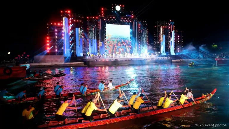 Traditional boats paddling in front of an illuminated riverfront stage in Can Tho