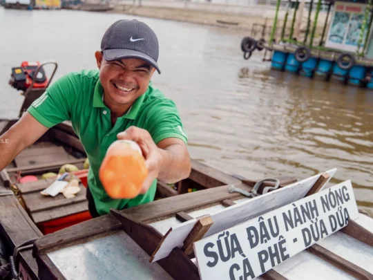 A friendly local vendor smiling from their boat at the Cai Rang Floating Market, offering a warm welcome to visitors.