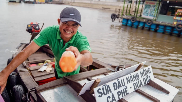 A friendly local vendor smiling from their boat at the Cai Rang Floating Market, offering a warm welcome to visitors.