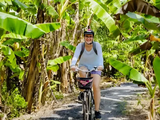 A person cycling along a quiet, tree-lined village road in the Mekong Delta, a popular activity on the Can Tho rural tour.