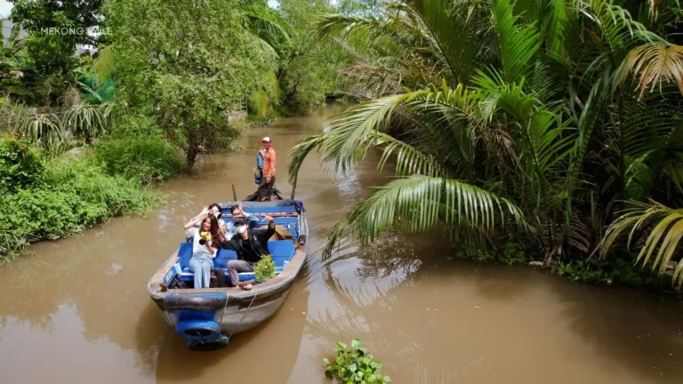 A traditional sampan boat navigating a tranquil, narrow canal shaded by palm trees on the Can Tho small canal tour