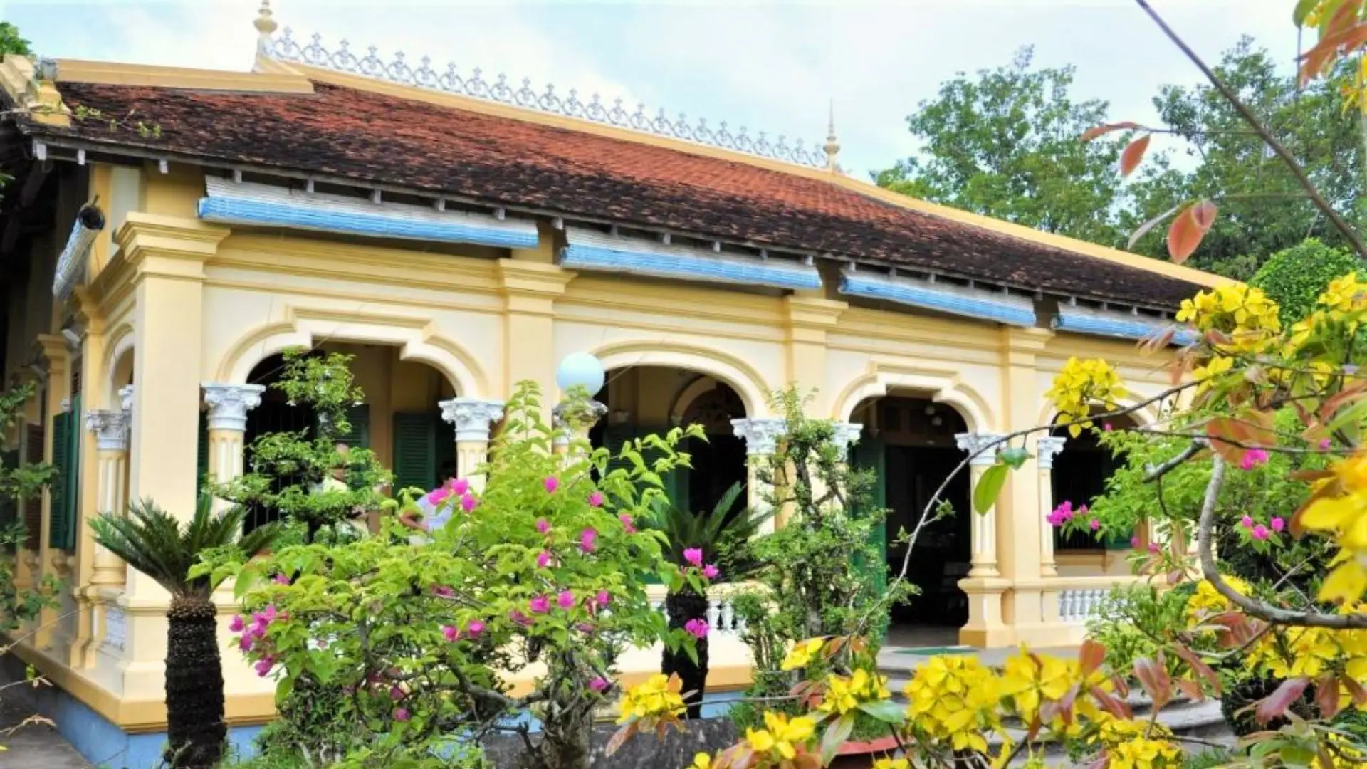 The ornate yellow facade and arched windows of Ba Duc Ancient House in Cai Be