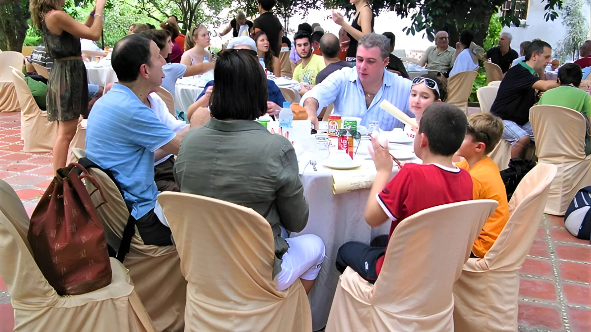 A group of international tourists enjoying a traditional Vietnamese dinner at long tables in the courtyard of Ba Duc Ancient House