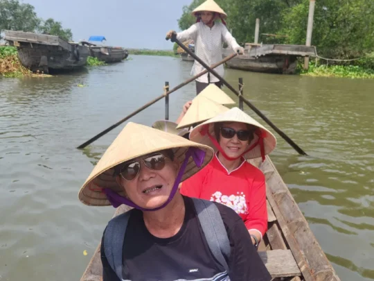 Two tourists wearing conical hats on a small boat in Cai Be