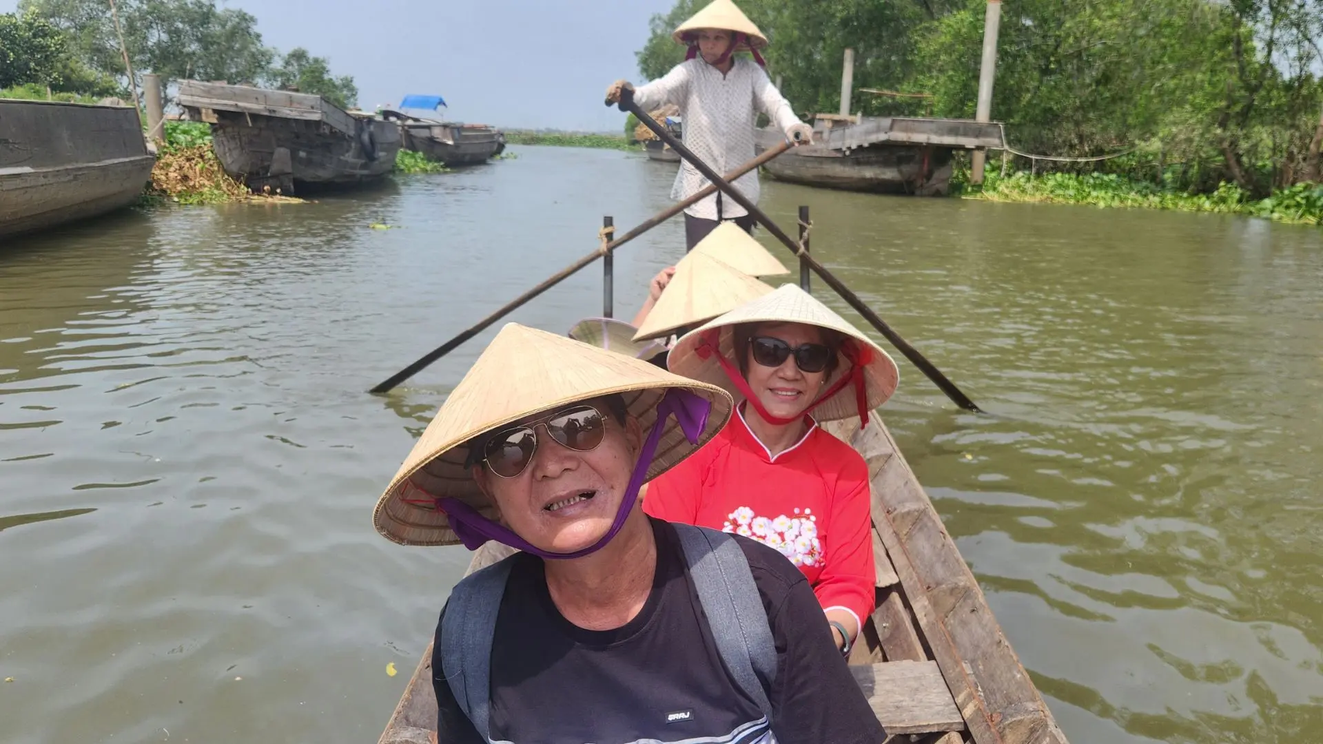 Two tourists wearing conical hats on a small boat in Cai Be