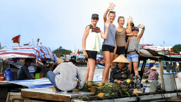 Mekong Smile Cai Be Floating Market tourists standing on vendor boat interacting with local sellers