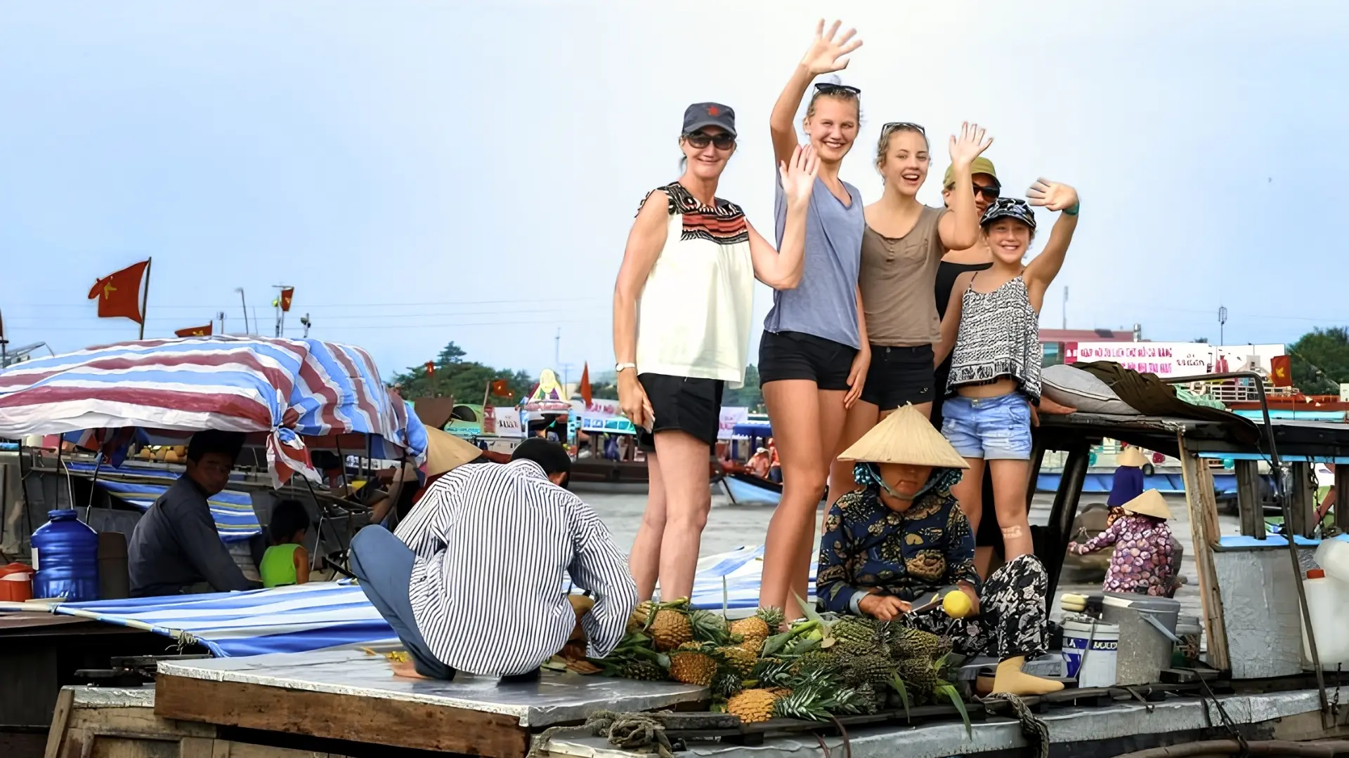 Mekong Smile Cai Be Floating Market tourists standing on vendor boat interacting with local sellers