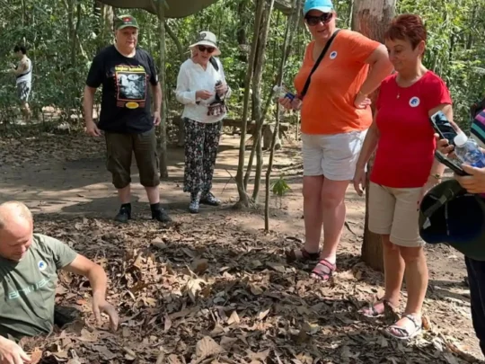 Tourist descending into the narrow tunnel opening at Cu Chi Tunnels Tour