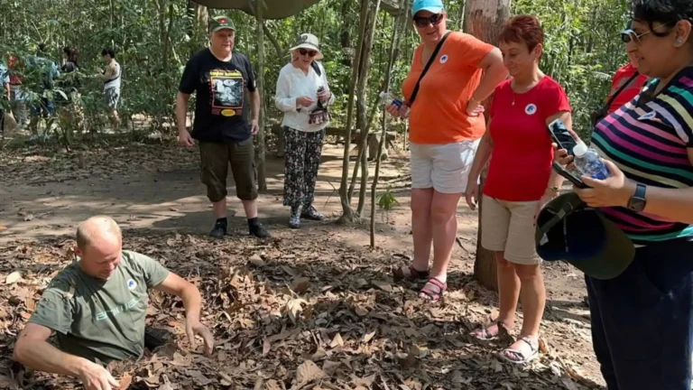 Tourist descending into the narrow tunnel opening at Cu Chi Tunnels Tour