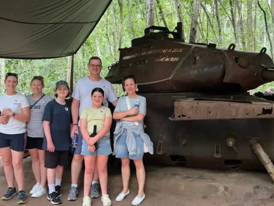 Family of tourists posing for a picture with a historical military tank in Cu Chi Tunnels Tour