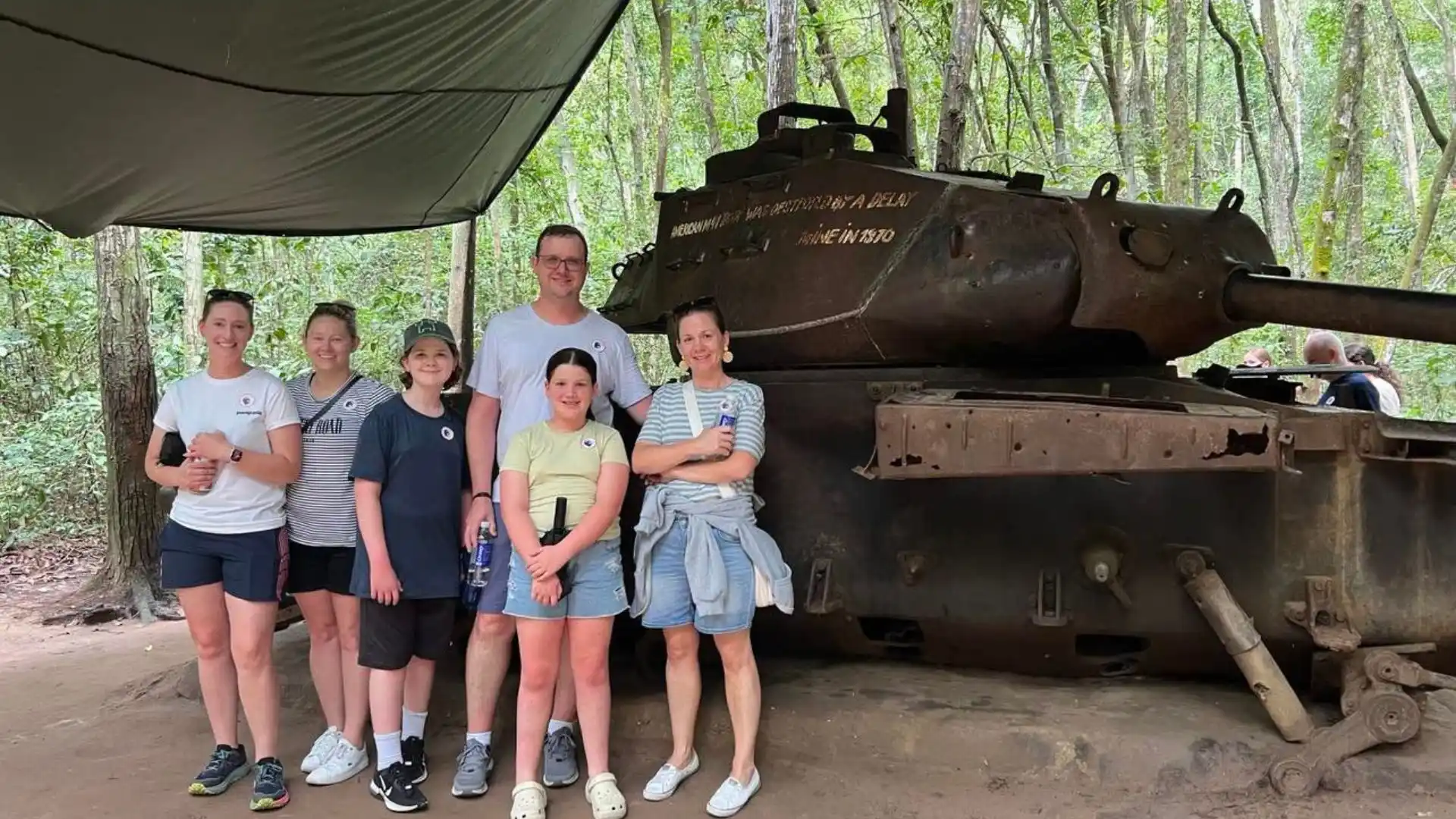 Family of tourists posing for a picture with a historical military tank in Cu Chi Tunnels Tour