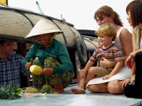 Guests experiencing cultural interaction with local vendors at Cai Rang Floating Market during a Mekong Delta cruise in Can Tho, Vietnam