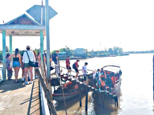Tourists descending wooden steps to board a boat for the Mekong Delta tour