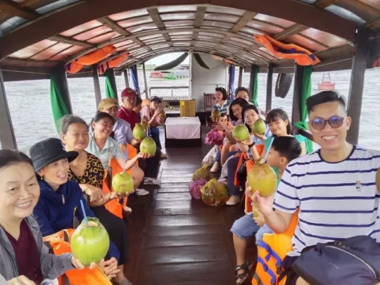 Tourist enjoying a fresh coconut drink on a boat during the Cai Be Tour