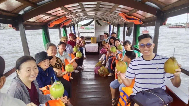 Tourist enjoying a fresh coconut drink on a boat during the Cai Be Tour