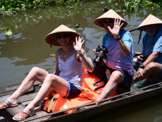 Tourist taking a photo of the scenery while riding on a small sampan boat in Mekong Delta Tour Cai Be