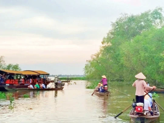 Hand-rowed sampan carrying tourists through a narrow, tree-shaded canal in Mekong Delta Tour Cai Be