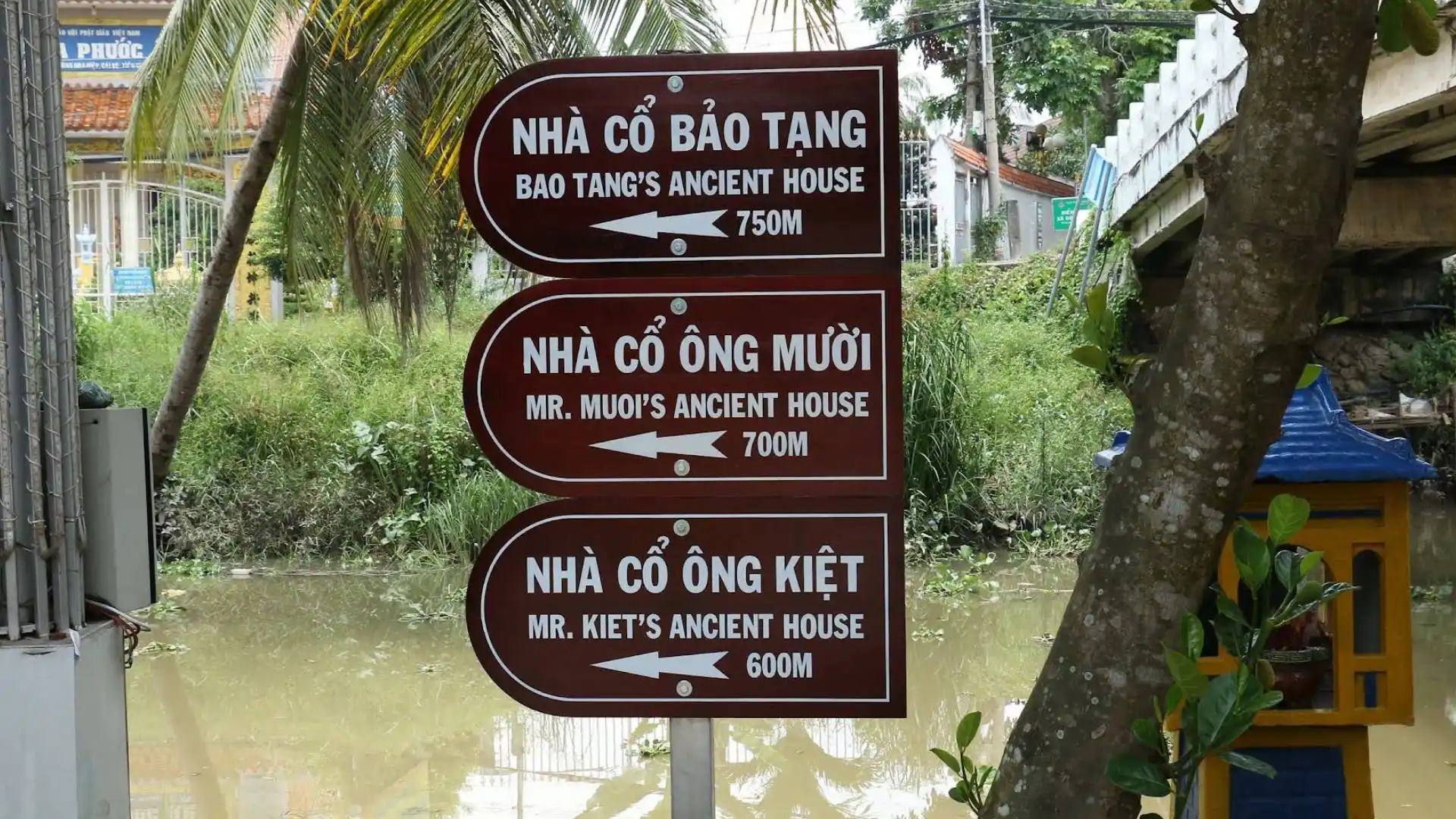A directional sign showing the distance to Mr Kiet Ancient House next to a Mekong river channel